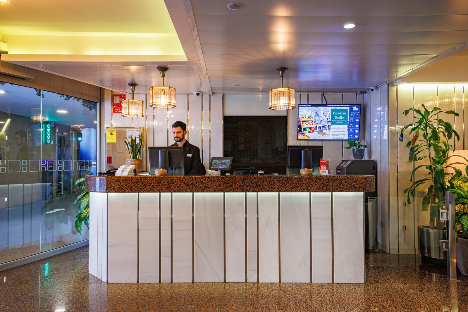 Receptionist welcoming guests at the green-walled reception desk of Hotel Ronda Lesseps, Gràcia Barcelona
